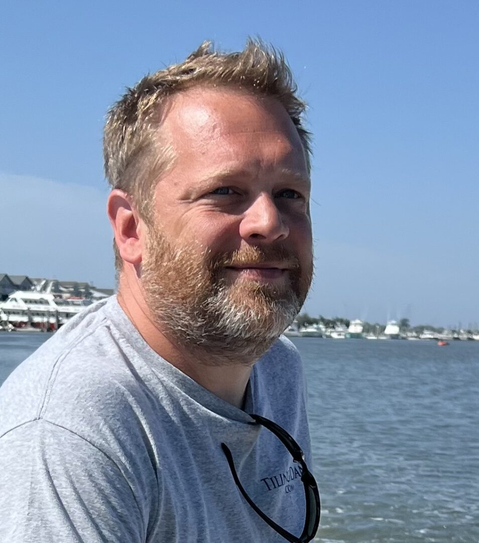 Man with beard smiling by the water.